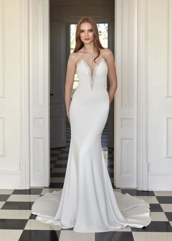 alt='Această rochie de mireasă tip sirenă din crep, cu decolteu în V, este o odă adusă rafinamentului. Designul său curat și elegant pune subtil silueta în valoare, în timp ce mărgelele adaugă o strălucire rafinată.'